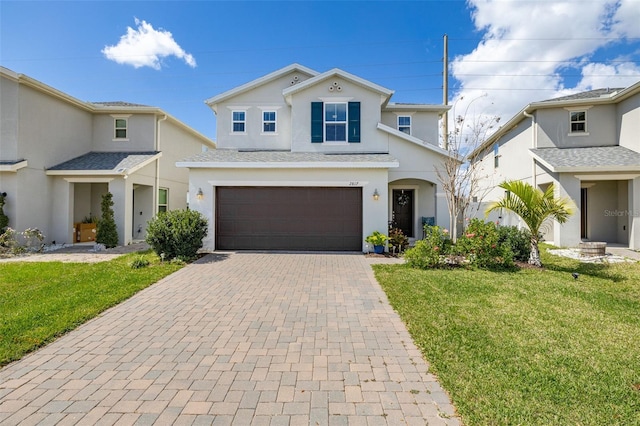 traditional home with decorative driveway, an attached garage, a front yard, and stucco siding