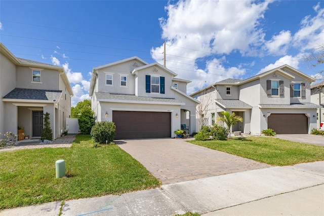 traditional-style home with a front lawn, decorative driveway, an attached garage, and stucco siding