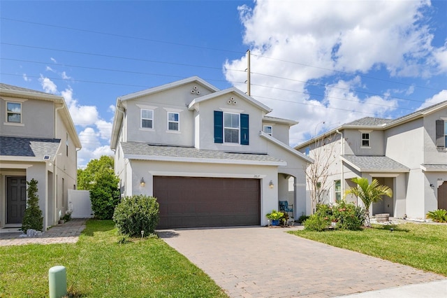 traditional-style house with decorative driveway, stucco siding, a shingled roof, a front yard, and a garage