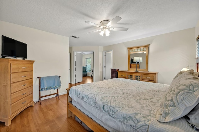 bedroom featuring visible vents, a ceiling fan, a textured ceiling, wood finished floors, and baseboards