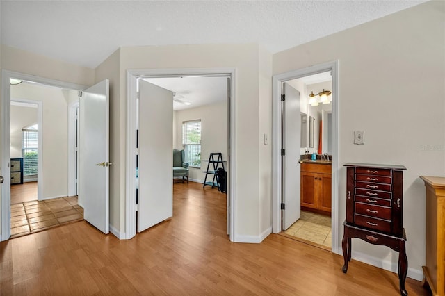 hall with a textured ceiling, light wood-type flooring, and baseboards