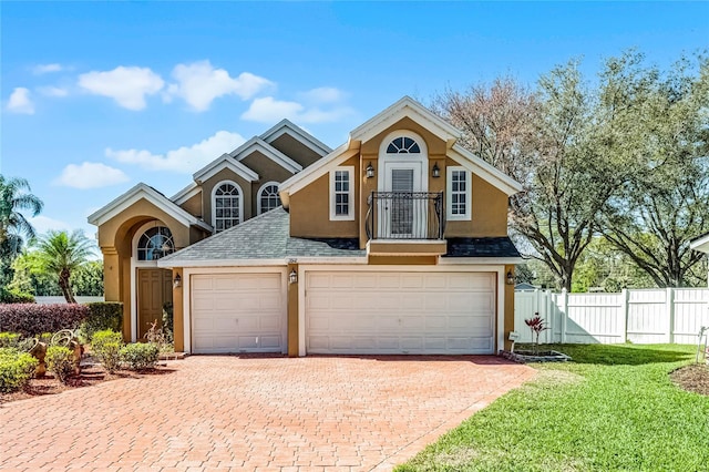 traditional-style home with decorative driveway, roof with shingles, stucco siding, fence, and a front lawn