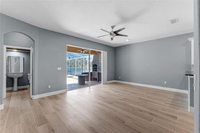 unfurnished living room featuring ceiling fan, baseboards, arched walkways, and light wood-style floors