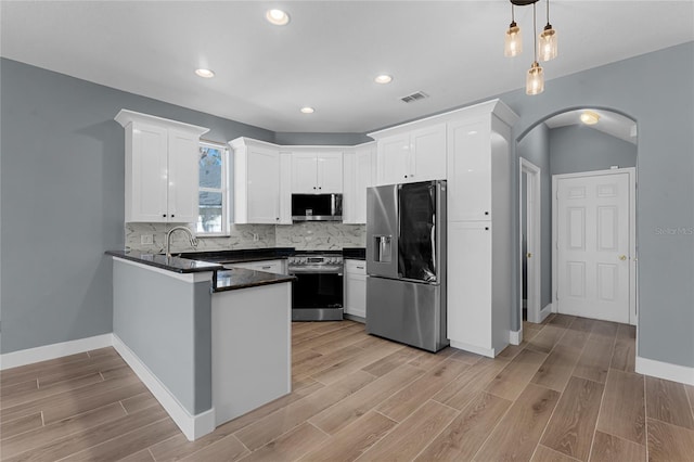 kitchen with tasteful backsplash, arched walkways, dark countertops, a peninsula, and stainless steel appliances