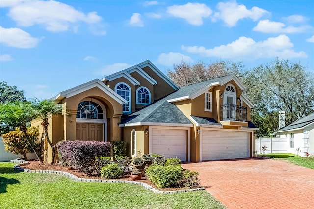 traditional-style house featuring roof with shingles, an attached garage, fence, decorative driveway, and stucco siding