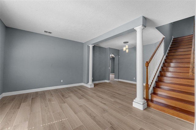 empty room featuring visible vents, baseboards, stairs, light wood finished floors, and ornate columns