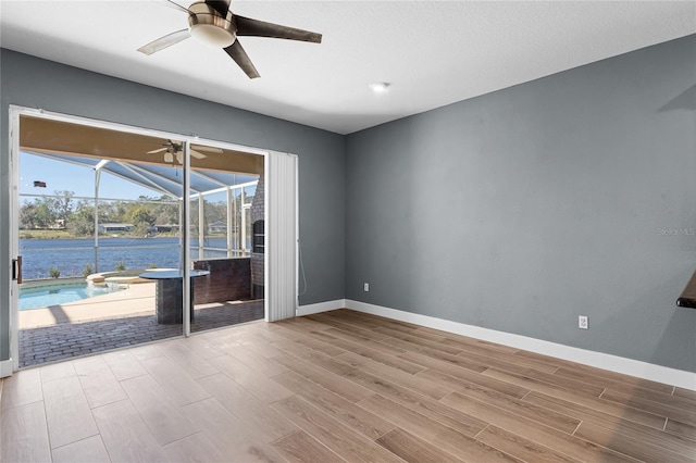 unfurnished room featuring a water view, a sunroom, baseboards, and wood finished floors