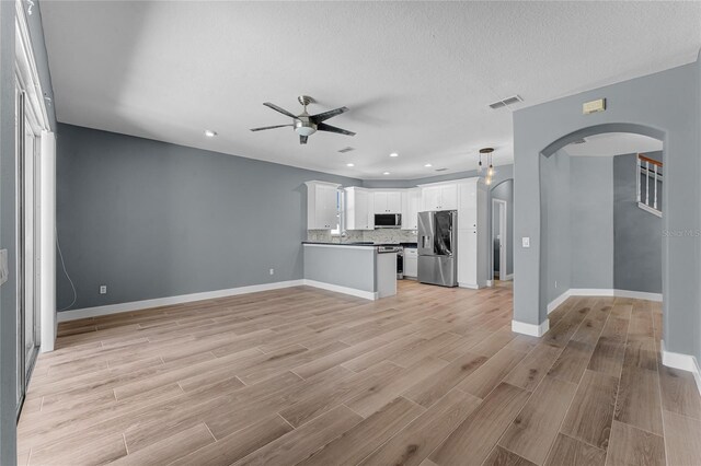 unfurnished living room featuring light wood finished floors, baseboards, visible vents, arched walkways, and a ceiling fan