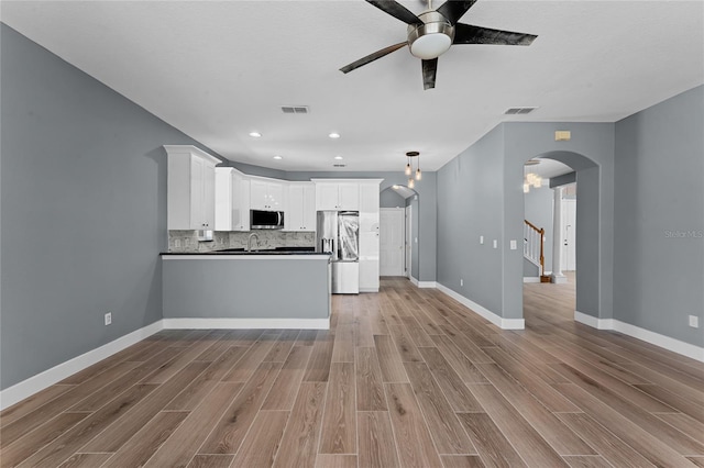 kitchen with appliances with stainless steel finishes, arched walkways, light wood-style flooring, and dark countertops