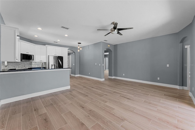 kitchen with arched walkways, a ceiling fan, dark countertops, open floor plan, and stainless steel appliances