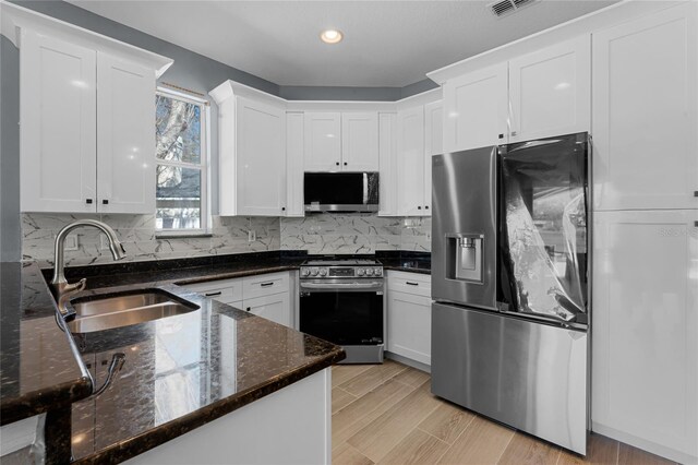 kitchen featuring white cabinets, appliances with stainless steel finishes, decorative backsplash, and a sink