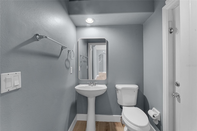 half bathroom featuring wood finished floors, toilet, and baseboards