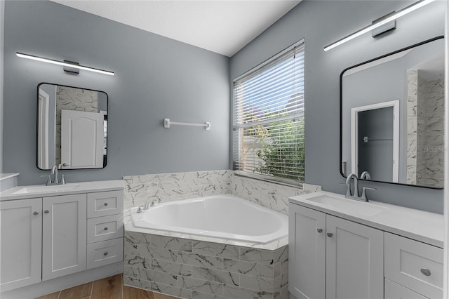 full bath featuring a garden tub, two vanities, and a sink