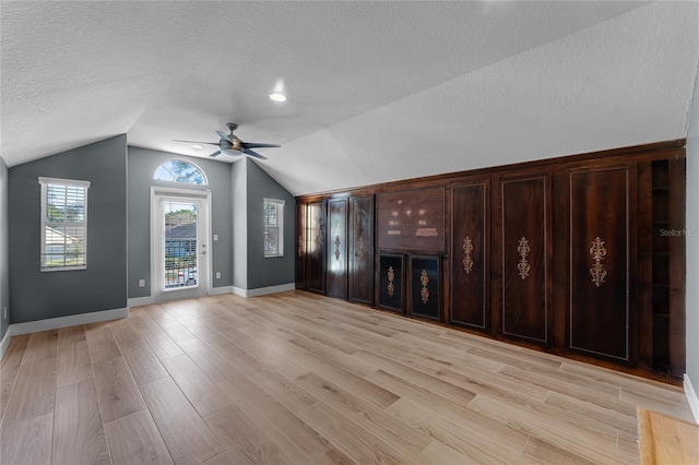 unfurnished living room with light wood-type flooring, vaulted ceiling, and a textured ceiling