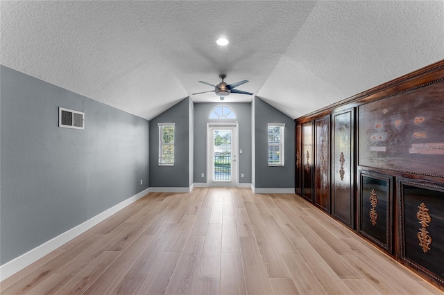 entryway with lofted ceiling, a textured ceiling, visible vents, a ceiling fan, and light wood-type flooring