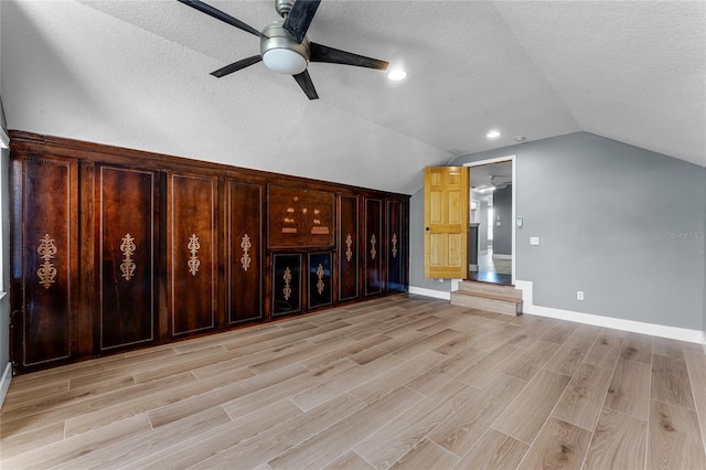 interior space featuring lofted ceiling, light wood-style flooring, ceiling fan, a textured ceiling, and baseboards