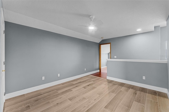 unfurnished room with ceiling fan, a textured ceiling, lofted ceiling, baseboards, and light wood-style floors