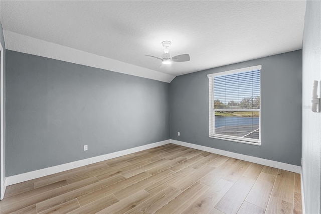 spare room with vaulted ceiling, light wood-style flooring, and baseboards