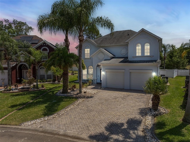 view of front of property with an attached garage, fence, decorative driveway, a lawn, and stucco siding