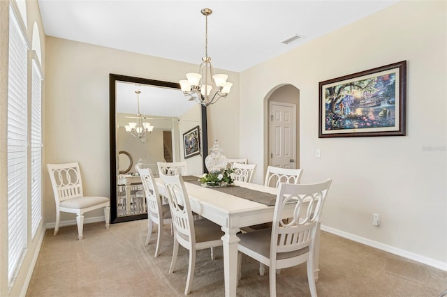 dining area featuring a chandelier, baseboards, arched walkways, and light colored carpet