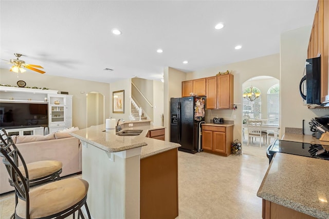 kitchen featuring black appliances, a kitchen bar, arched walkways, and a sink