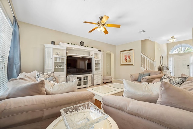 living area featuring baseboards, stairs, visible vents, and a ceiling fan