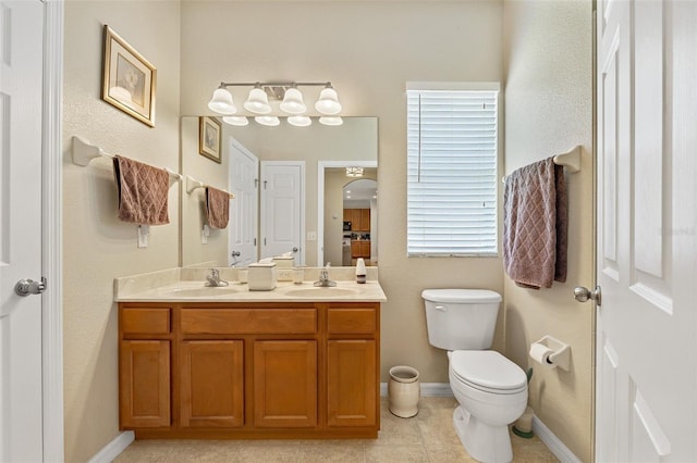 bathroom with double vanity, baseboards, toilet, and a sink