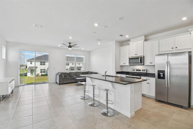 kitchen featuring dark countertops, appliances with stainless steel finishes, open floor plan, white cabinetry, and a sink