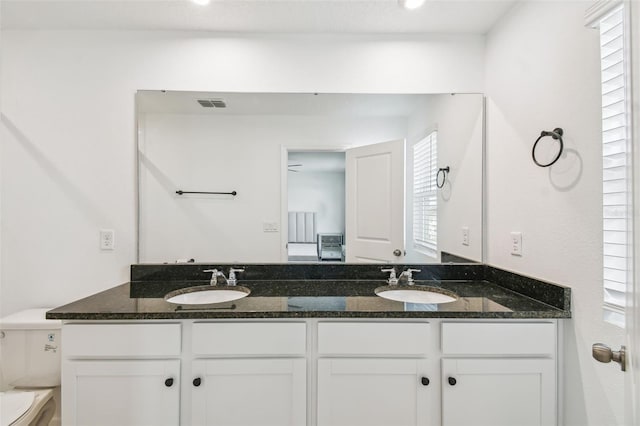 bathroom with toilet, double vanity, a sink, and visible vents