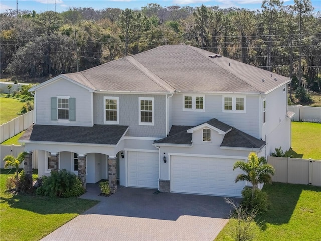 view of front of home with a front yard, fence, an attached garage, a shingled roof, and decorative driveway