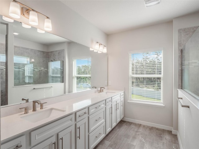 full bathroom with double vanity, wood finished floors, a tile shower, and a sink