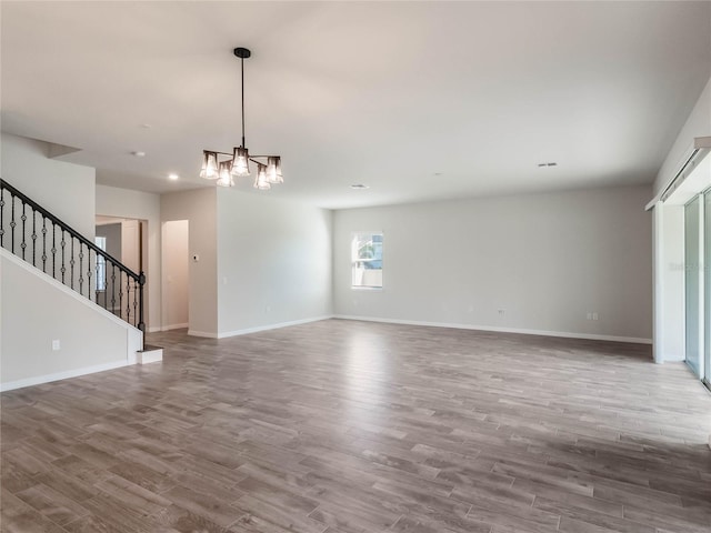 unfurnished living room with a notable chandelier, stairway, baseboards, and wood finished floors