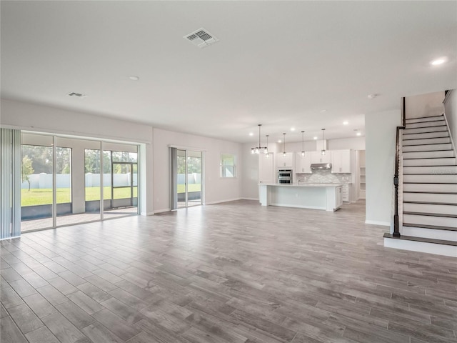 unfurnished living room featuring recessed lighting, visible vents, light wood finished floors, and stairway