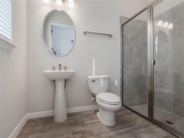 bathroom featuring a shower stall, toilet, wood finished floors, and baseboards