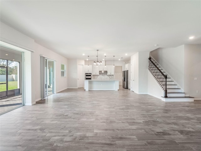 unfurnished living room with recessed lighting, light wood-type flooring, stairs, and baseboards