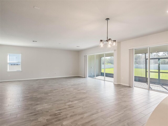 empty room featuring a notable chandelier, baseboards, and wood finished floors