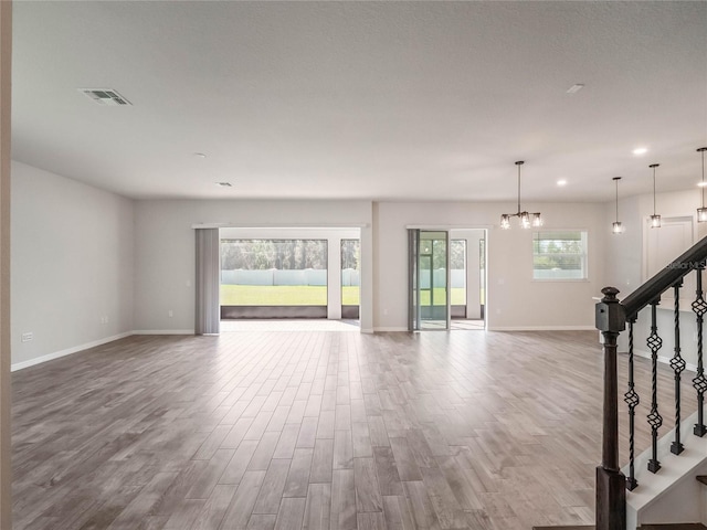 unfurnished living room featuring stairway, wood finished floors, visible vents, baseboards, and an inviting chandelier