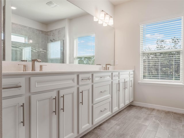 bathroom with a wealth of natural light, baseboards, tiled shower, and double vanity