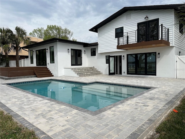 rear view of property featuring fence, entry steps, stucco siding, a balcony, and a patio