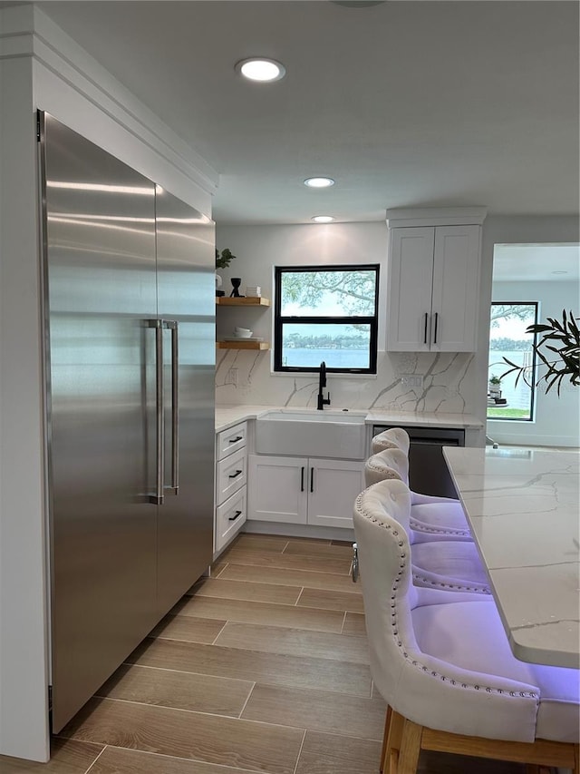 kitchen with built in refrigerator, decorative backsplash, a sink, open shelves, and dishwashing machine