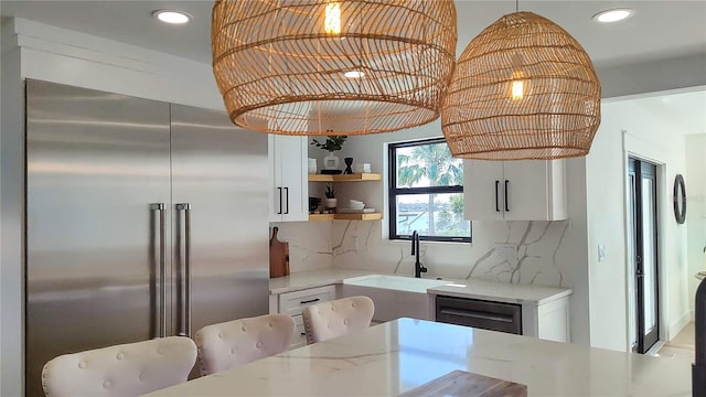 kitchen with tasteful backsplash, white cabinetry, high quality fridge, and a sink