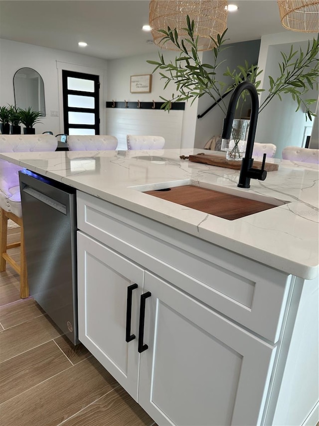 kitchen featuring light stone countertops, white cabinetry, wood finish floors, a sink, and dishwasher