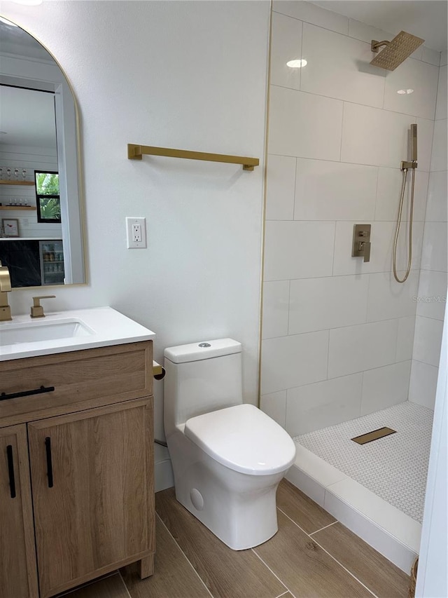 bathroom featuring wood finish floors, tiled shower, toilet, and vanity