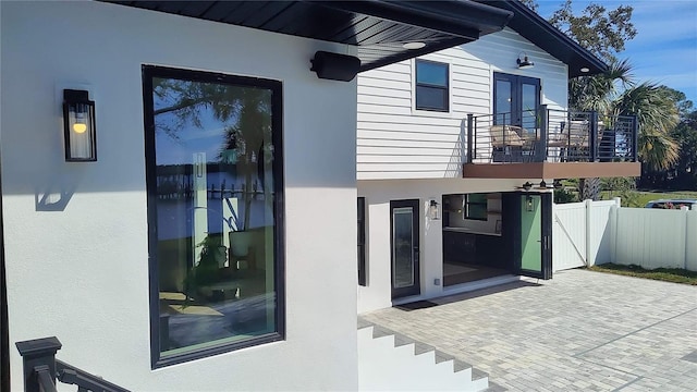 doorway to property with a balcony, fence, stucco siding, french doors, and a patio area