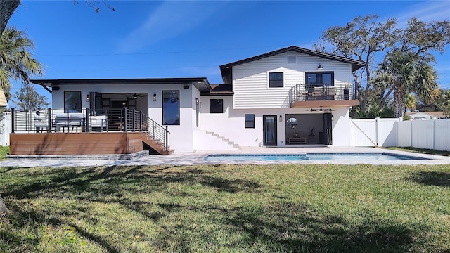 rear view of house featuring a fenced in pool, fence, stucco siding, a lawn, and a balcony