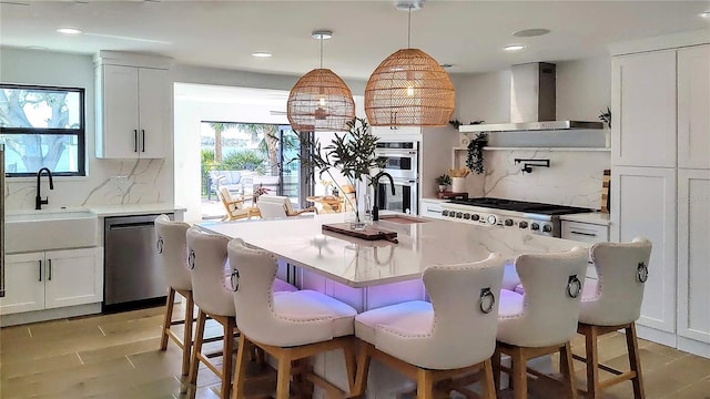 kitchen featuring white cabinetry, stainless steel appliances, wall chimney range hood, and a sink