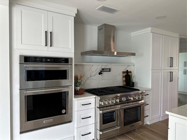 kitchen with wood finished floors, visible vents, decorative backsplash, appliances with stainless steel finishes, and wall chimney range hood