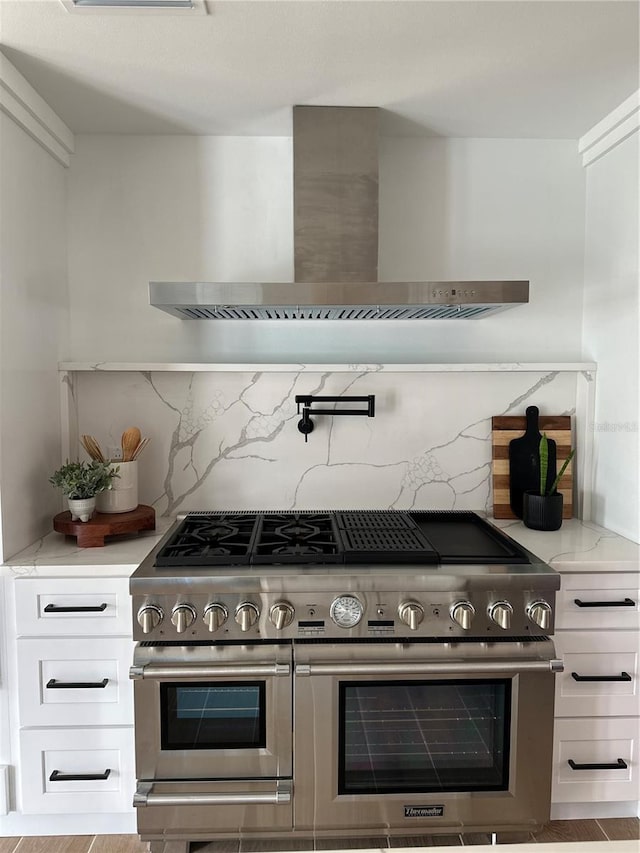 kitchen with tasteful backsplash, wall chimney range hood, double oven range, light stone counters, and white cabinets