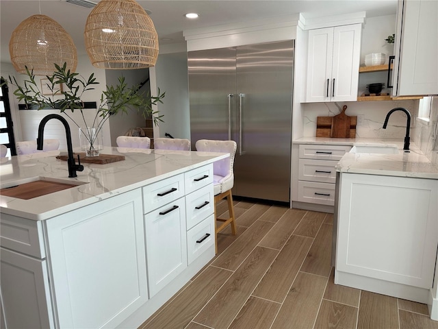 kitchen with a sink, open shelves, built in fridge, and wood tiled floor