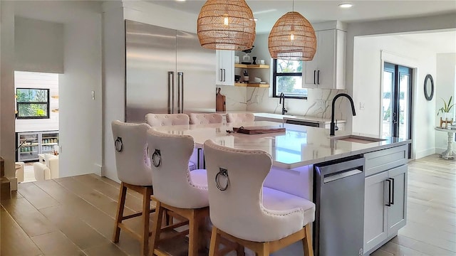 kitchen with backsplash, pendant lighting, an island with sink, appliances with stainless steel finishes, and a sink